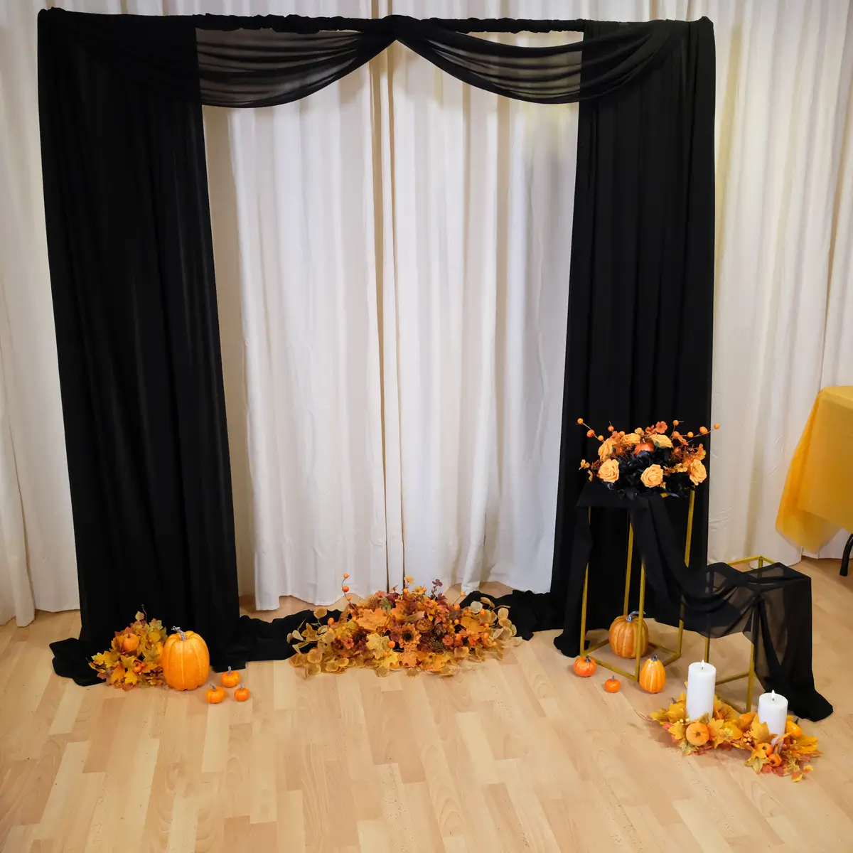 Backdrop med sort stof, orange blomsterdeko, græskar, firkant stativer og lyskranse