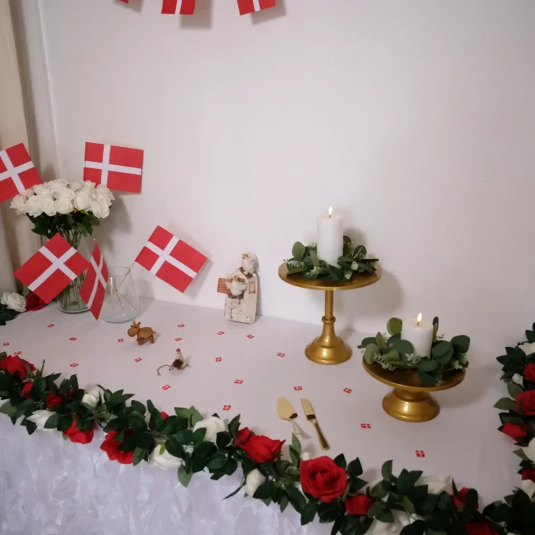 Gavebord med hvid tyl bordnederdel, røde og hvide rosenranker, LED stearinlys, eukalyptus blad kranse, gyldne kagestativer, guldfarvet kageskæringssæt, hvide roser og flag - fødselsdag - workcase