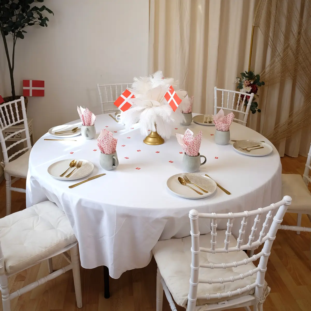 Spiseområde med glat guldbestik, hvid dug, stentøjstallerkener og krus, fjerdekoration og flag - fødselsdag - workcase